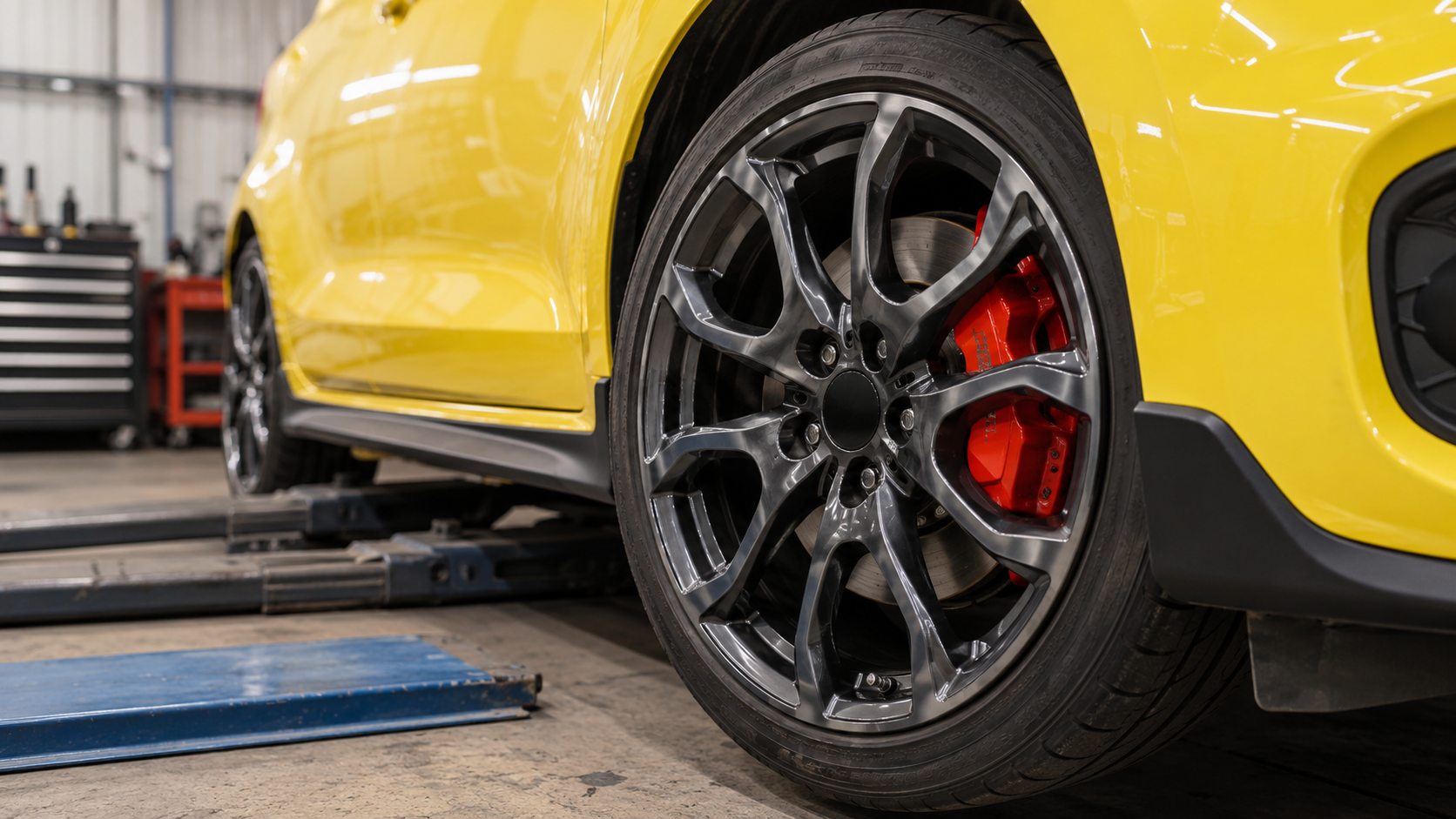 整備工場に置かれたイエローのスポーツ車のアルミホイールとブレーキキャリパー
