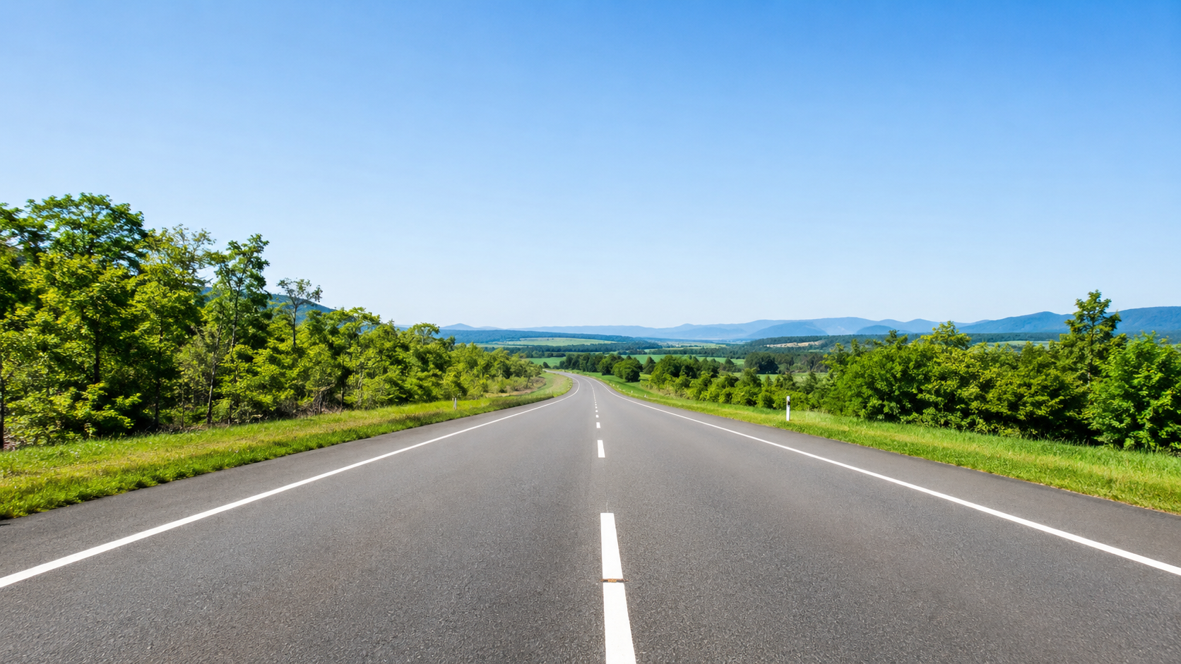 晴天の下、広い道路を走ることを想像させるような、遠くへと続く道の風景
